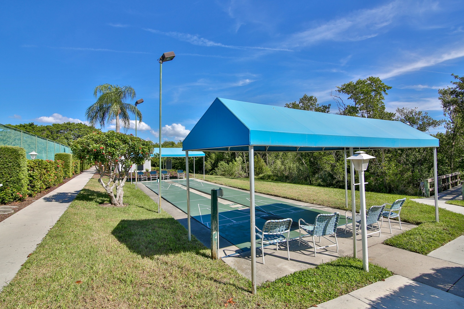 Community recreation area featuring covered seating and adjacent sports courts set amid landscaped grounds under sunny skies.