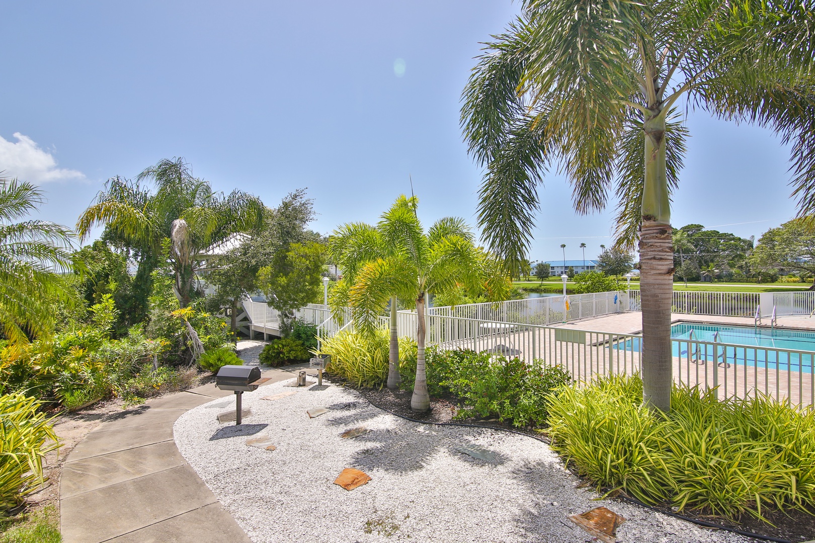 Lush tropical gardens frame a sparkling pool area, perfect for your sunny afternoon escape. A private BBQ station awaits your cookout under swaying palms.