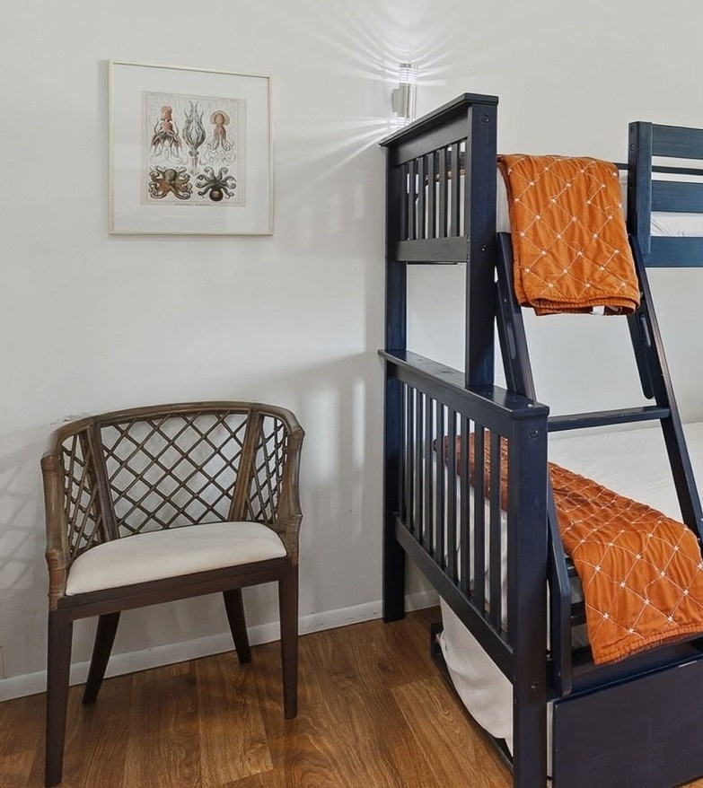 Your cozy bunk room features navy beds with vibrant orange bedding, a wicker reading chair, and ocean-themed art.
