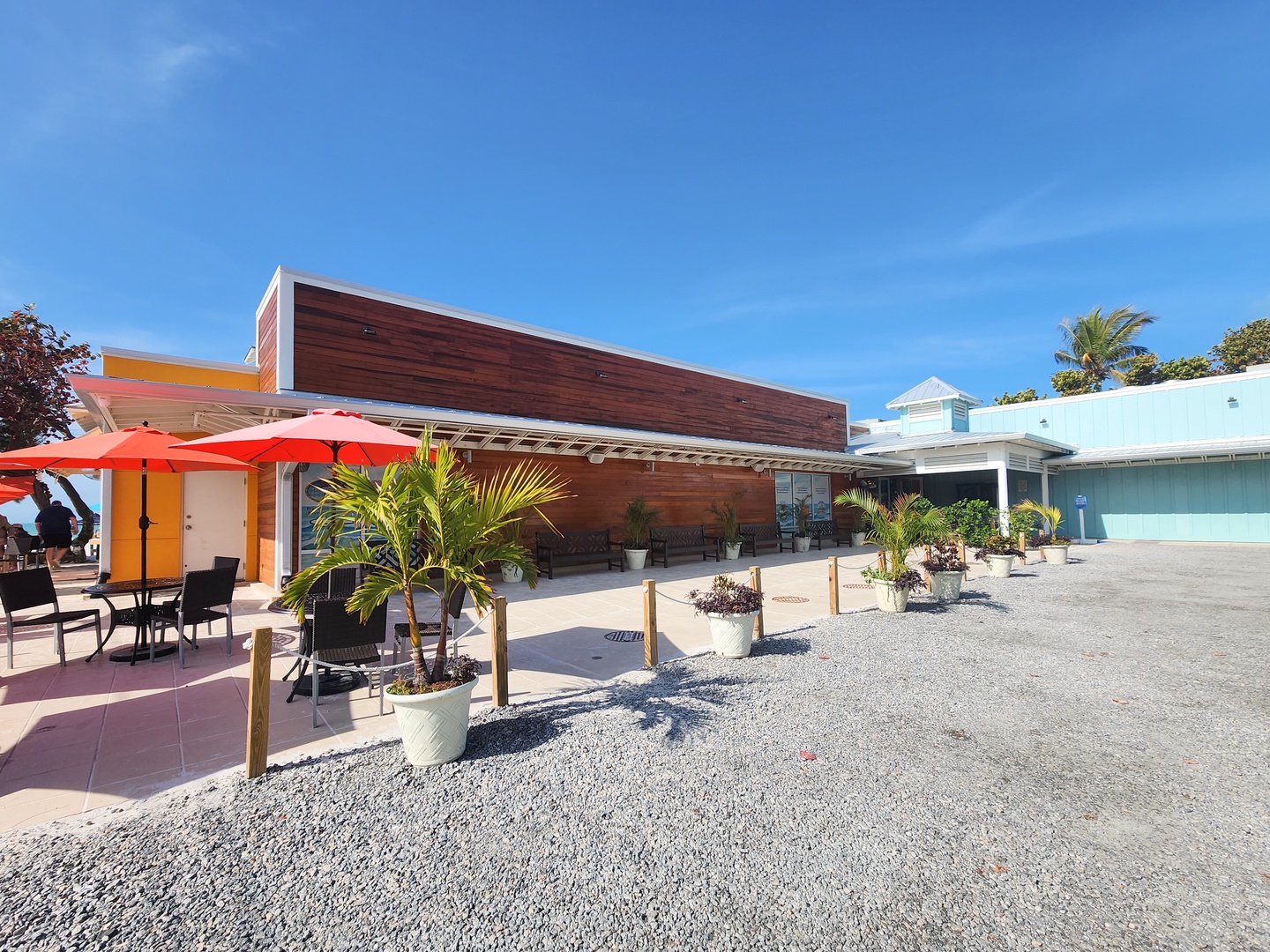 Modern beachfront property with tropical landscaping and outdoor dining areas under clear blue skies.