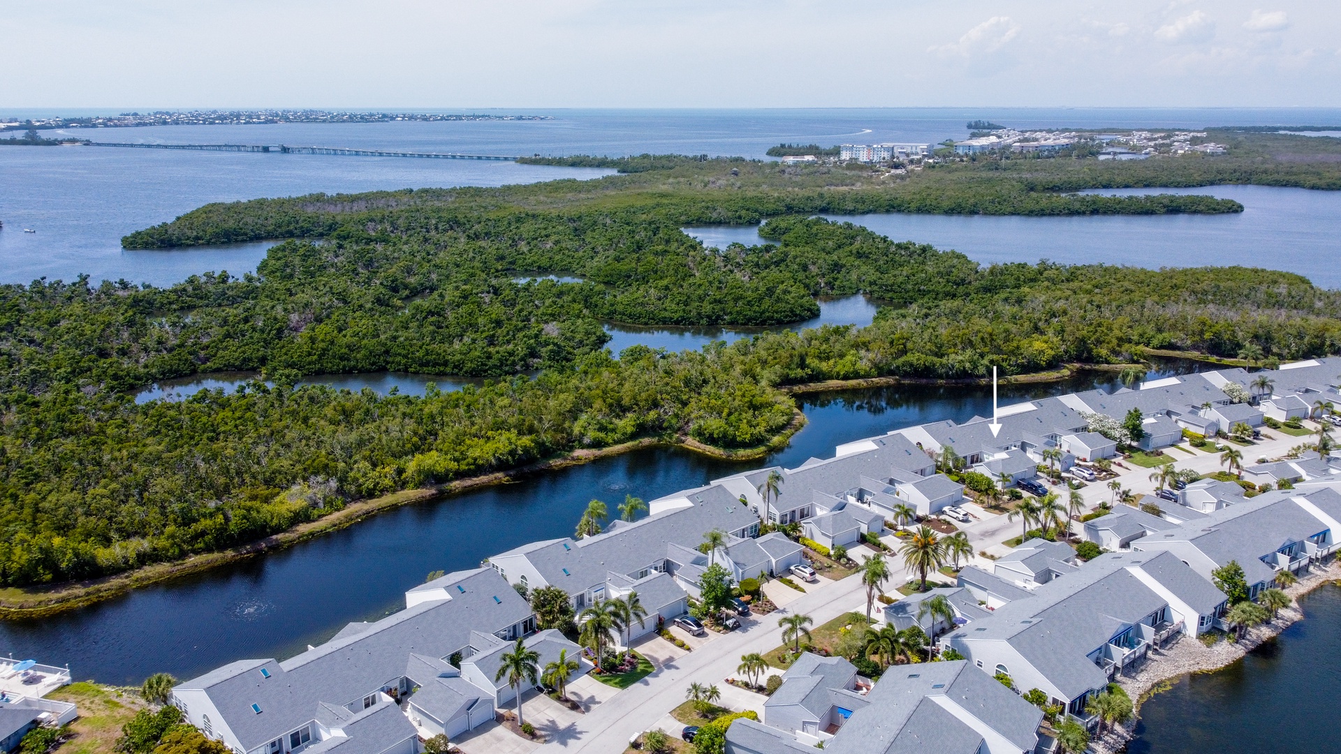 Aerial view of the property nestled along tranquil waterways, surrounded by lush mangroves and coastal scenery, with a bridge and ocean visible in the distance.