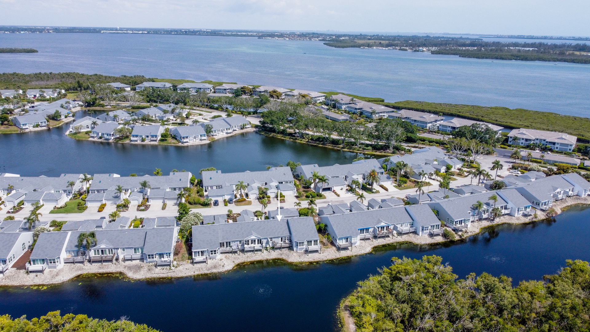 Aerial view of a waterfront residential community featuring modern homes along serene canal and bay access, surrounded by lush natural landscapes and expansive water views.