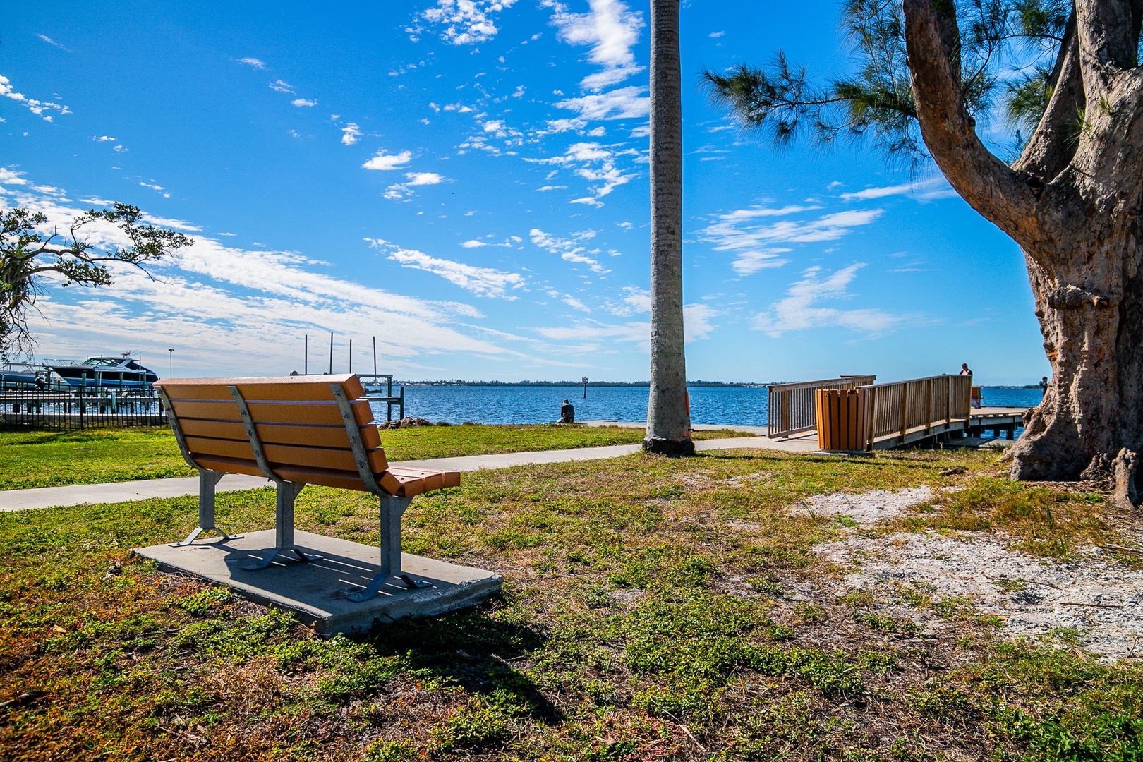 Waterfront park with bench and dock offers peaceful views of blue waters and distant marina.