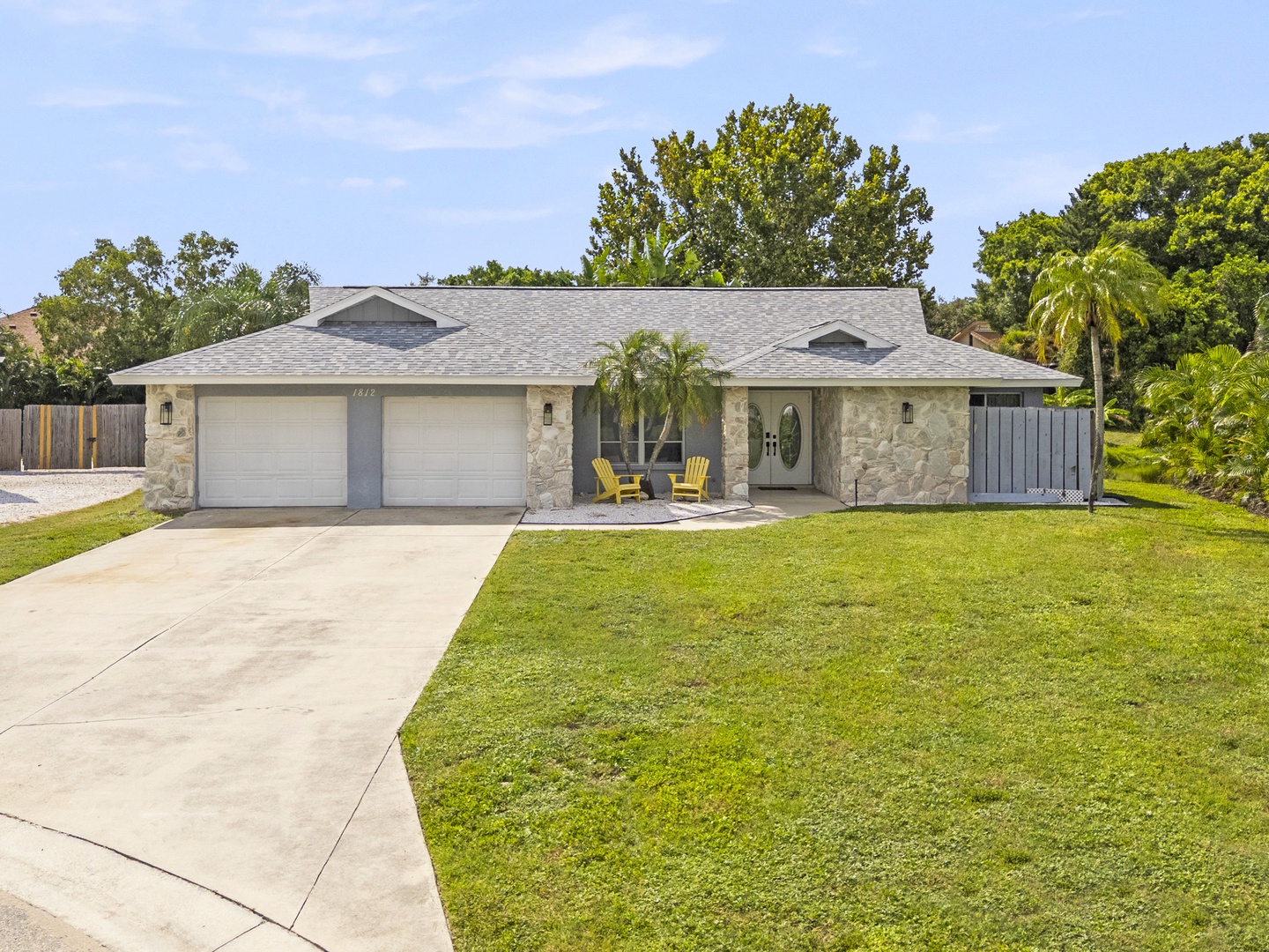 The property features a stone-accented facade with a welcoming covered entry and lush tropical landscaping, set in a quiet, established neighborhood.