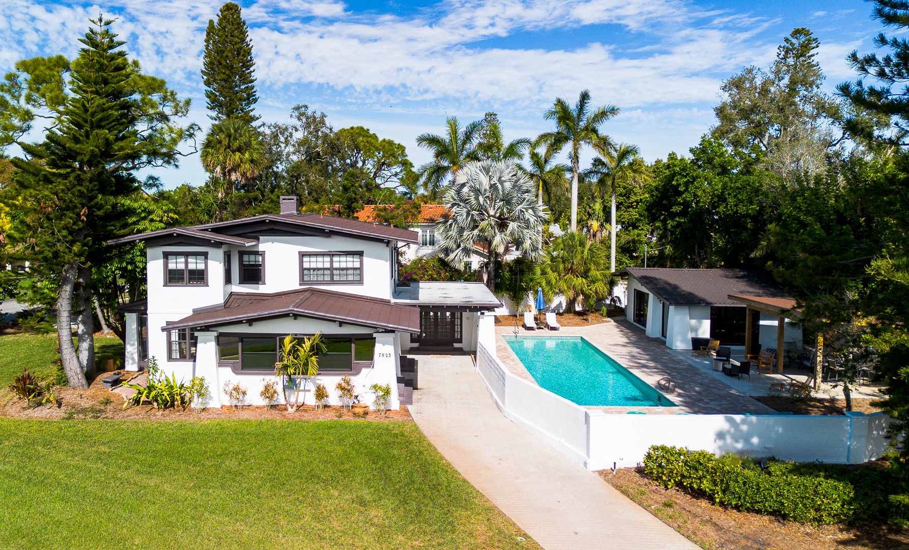 A stunning waterfront property featuring a sparkling swimming pool surrounded by lush tropical landscaping and mature palm trees.