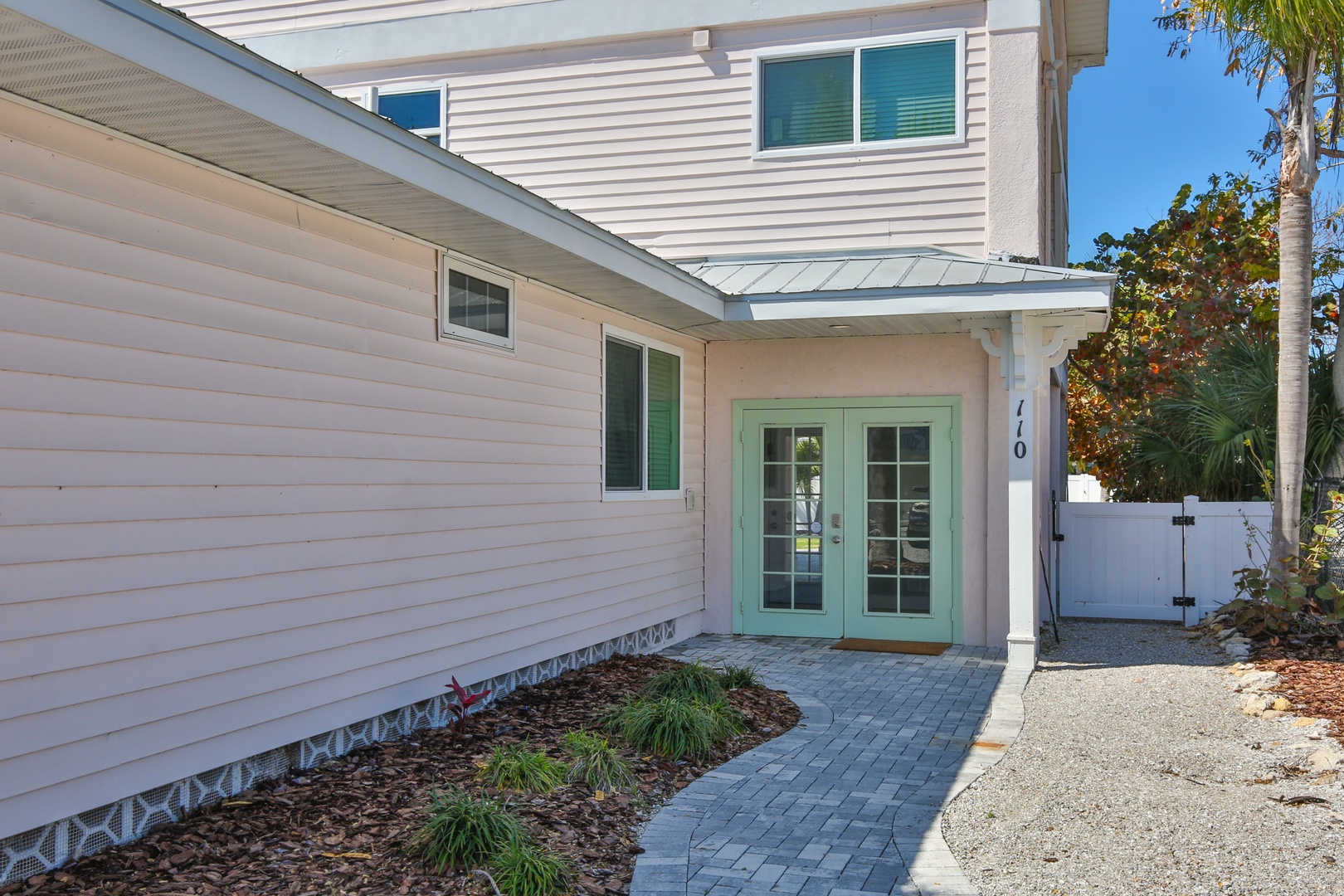 Modern coastal home with charming mint green entrance doors and tropical landscaping creates a welcoming arrival experience.