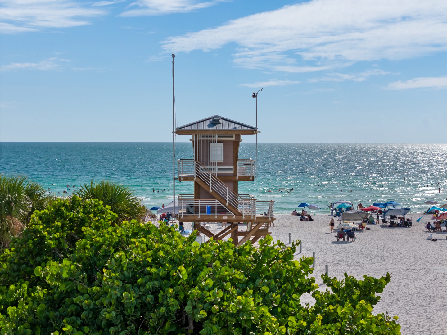Pristine beach with lifeguard tower, turquoise waters, and white sand where families gather under colorful umbrellas on sunny days.
