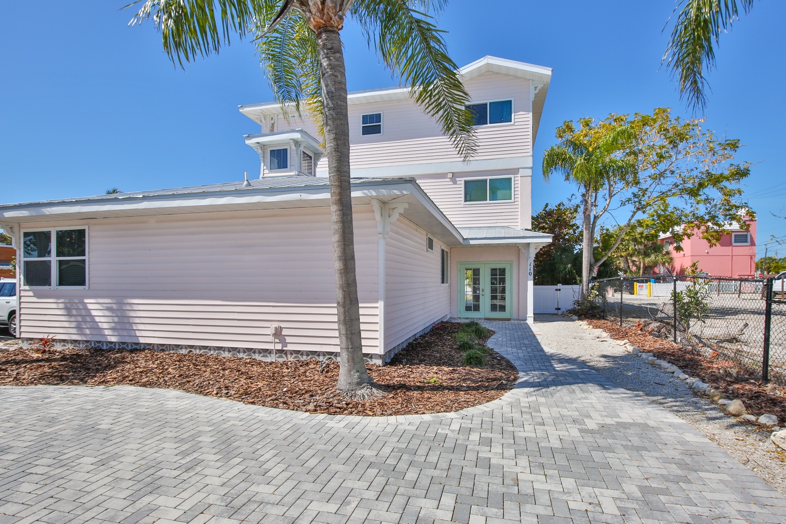 Modern beachside home with tropical landscaping and paved driveway in a residential coastal neighborhood.