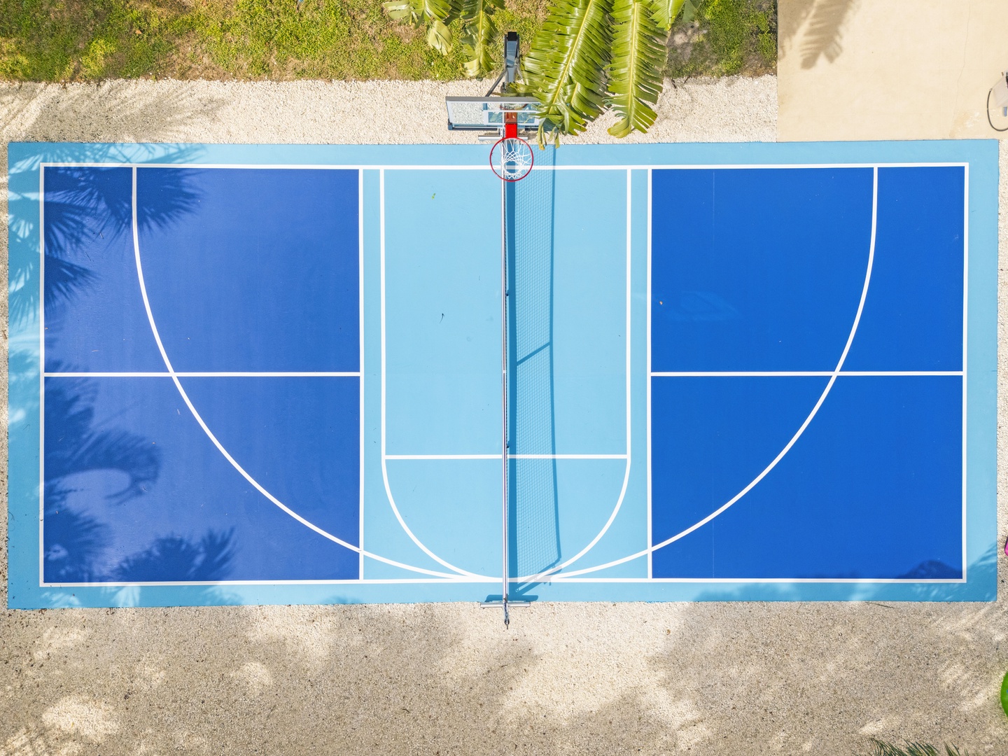 An aerial view of the property's blue basketball court, surrounded by tropical greenery and sandy areas, offering an active outdoor recreation option.