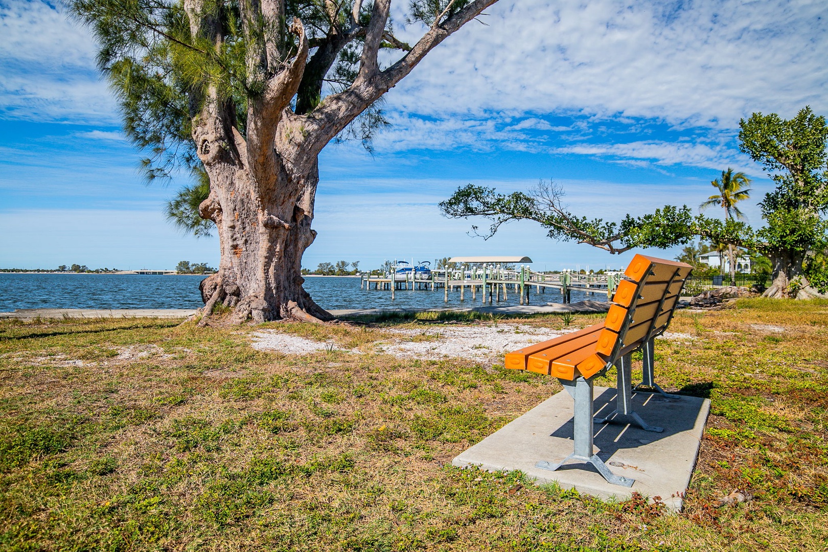 Waterfront park with orange bench overlooking tranquil bay waters and fishing pier under expansive blue skies.