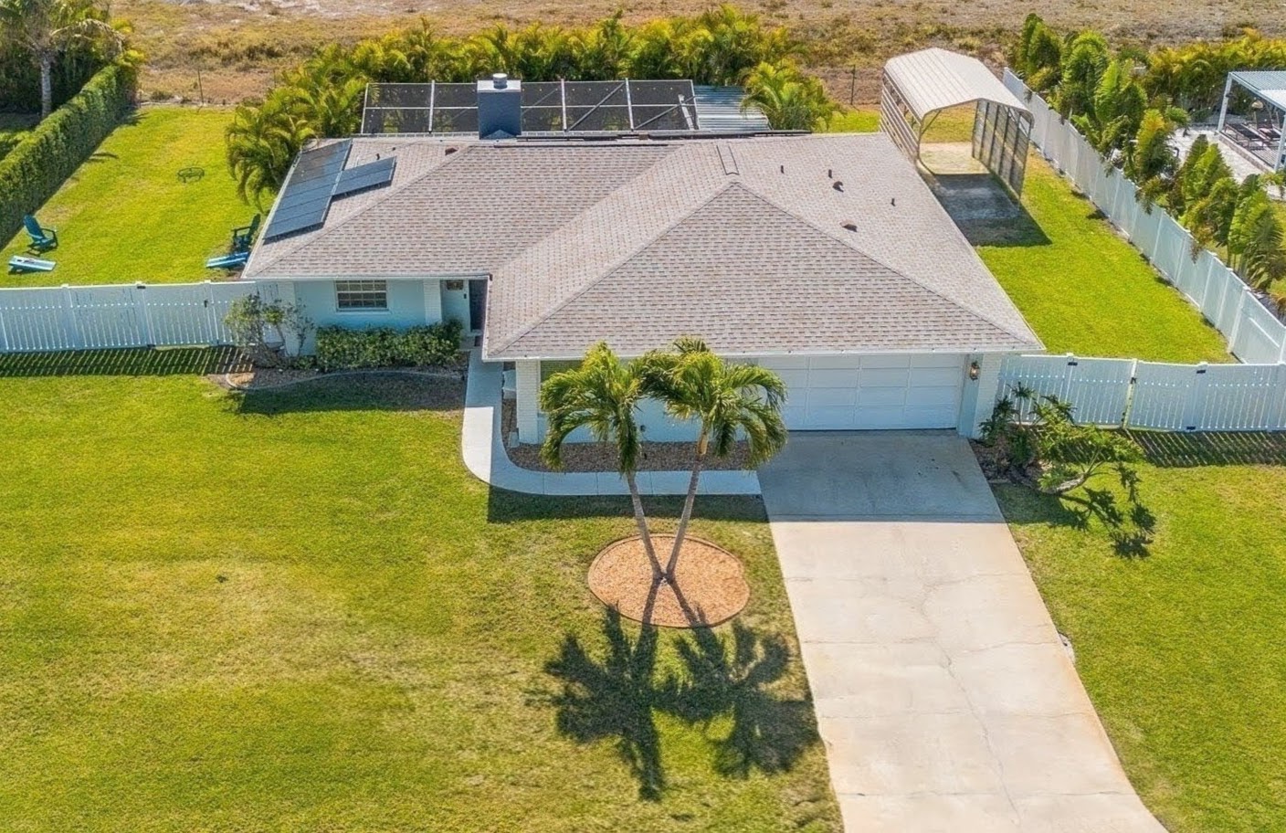 Aerial view of a single-story vacation home, surrounded by a spacious lawn and tropical landscaping in a peaceful residential neighborhood.