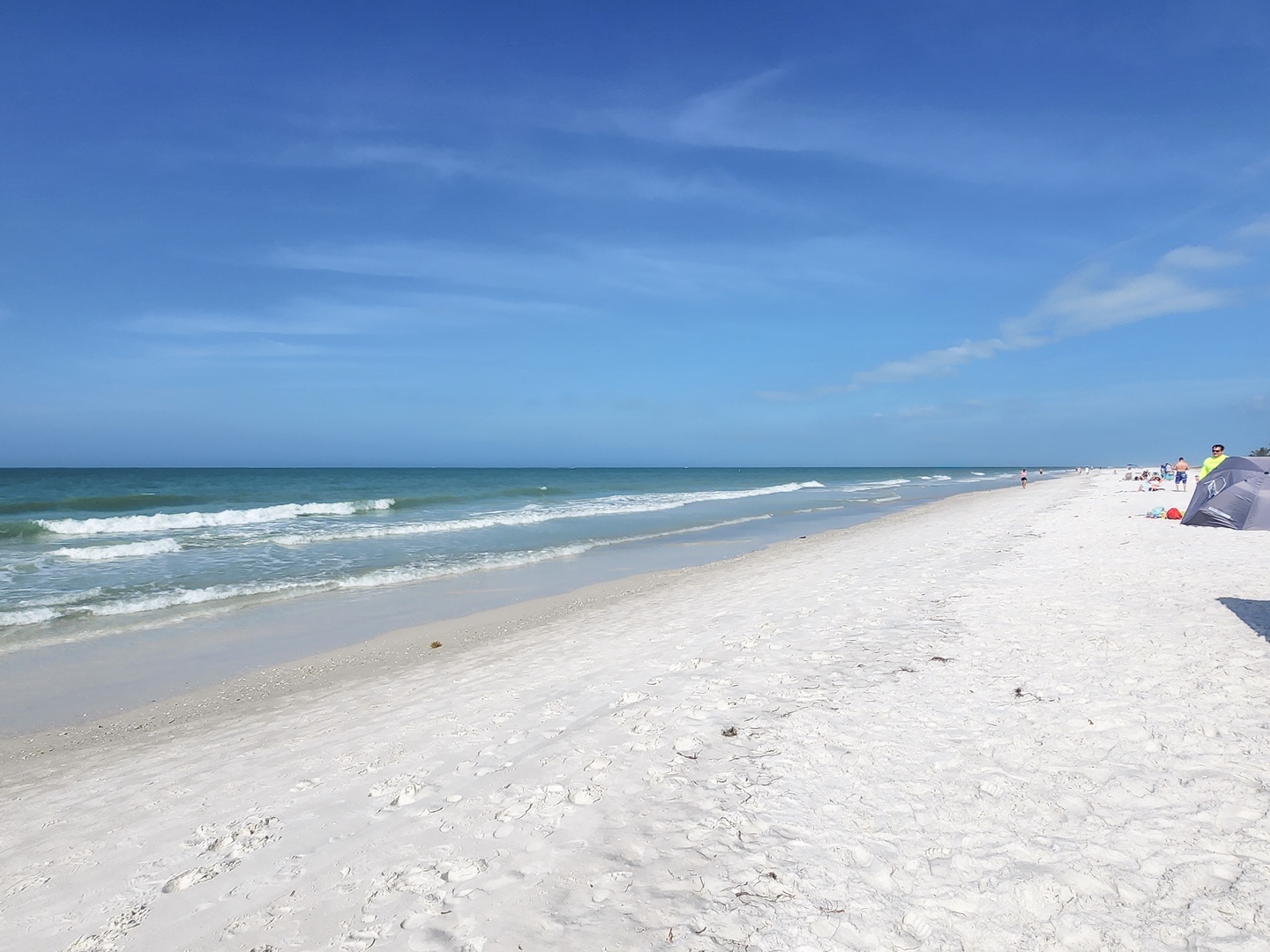 Pristine white sand beach stretches along turquoise waters under brilliant blue skies, offering endless shoreline for peaceful walks and relaxation.