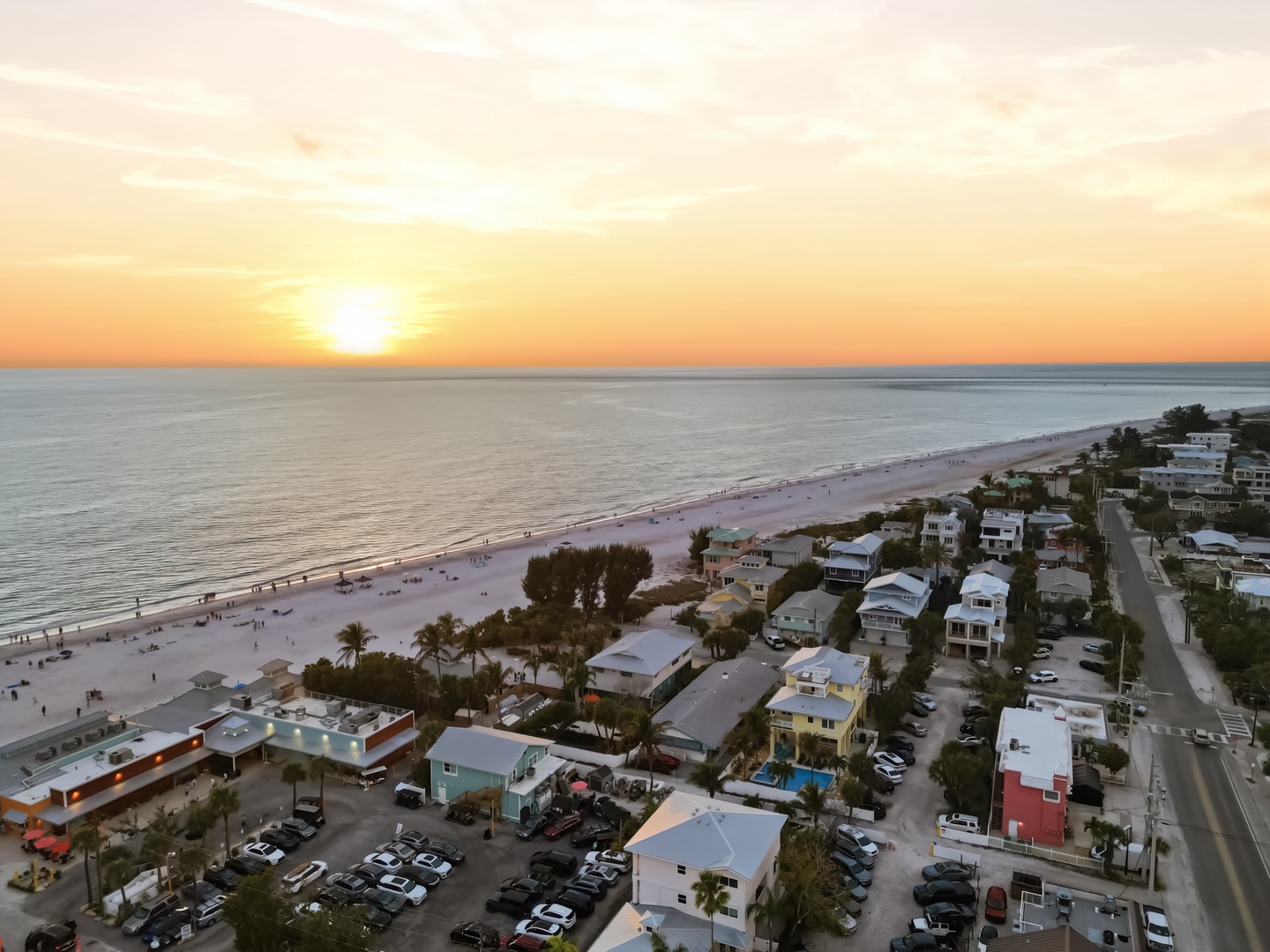 Stunning aerial view of beachfront community at sunset, showcasing pristine white sand beach and surrounding coastal neighborhood.