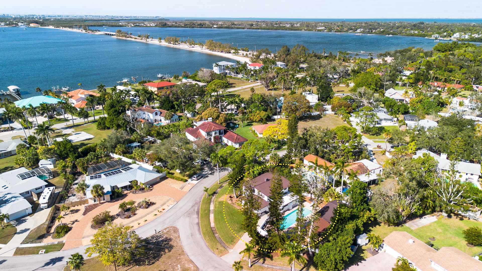 Aerial view of a waterfront residential community featuring tree-lined streets, diverse housing, and pristine bay access with sandy beaches.