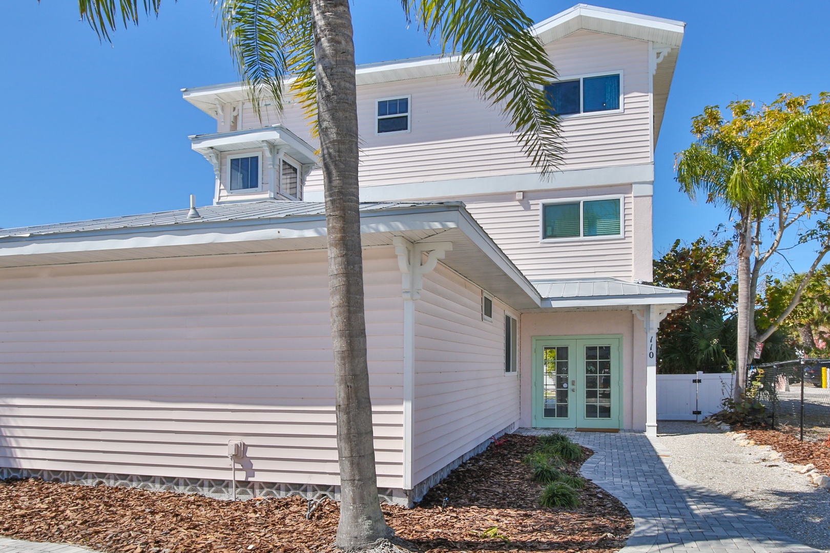 Modern coastal retreat featuring clean white siding, tropical palms, and a welcoming entrance surrounded by native landscaping under Florida's endless blue skies.