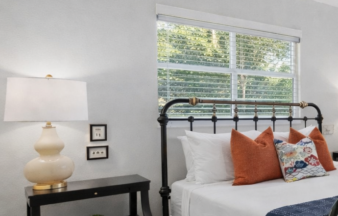 Sink into crisp white linens and colorful pillows while natural light streams through your window, creating the perfect retreat for peaceful mornings.