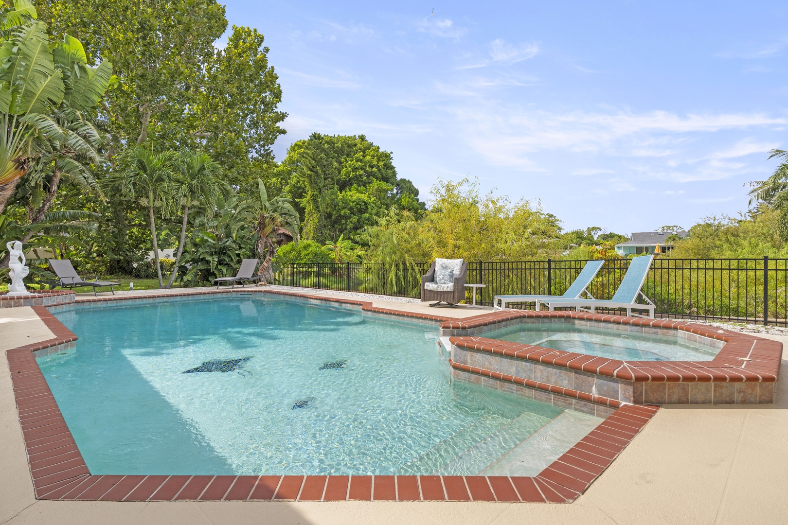 A spacious brick-lined pool surrounded by lush tropical landscaping and loungers. Step down into the attached spa, perfect for unwinding after exploring the area.