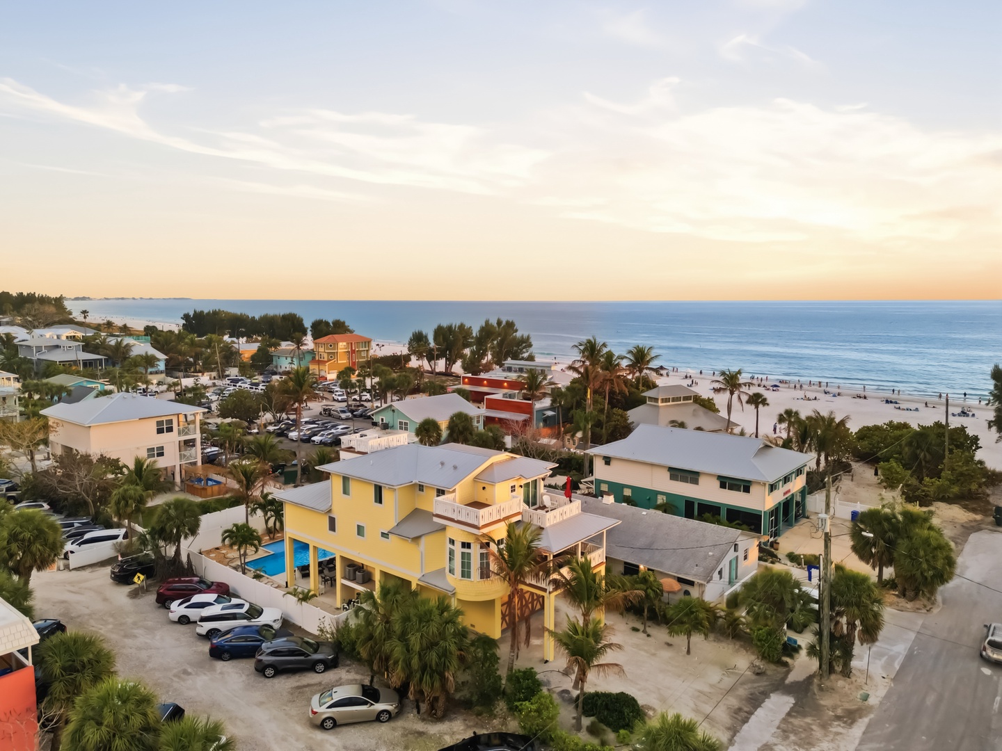 Tropical beachfront community with colorful buildings and pristine sandy shores stretching along crystal-clear waters at golden hour.