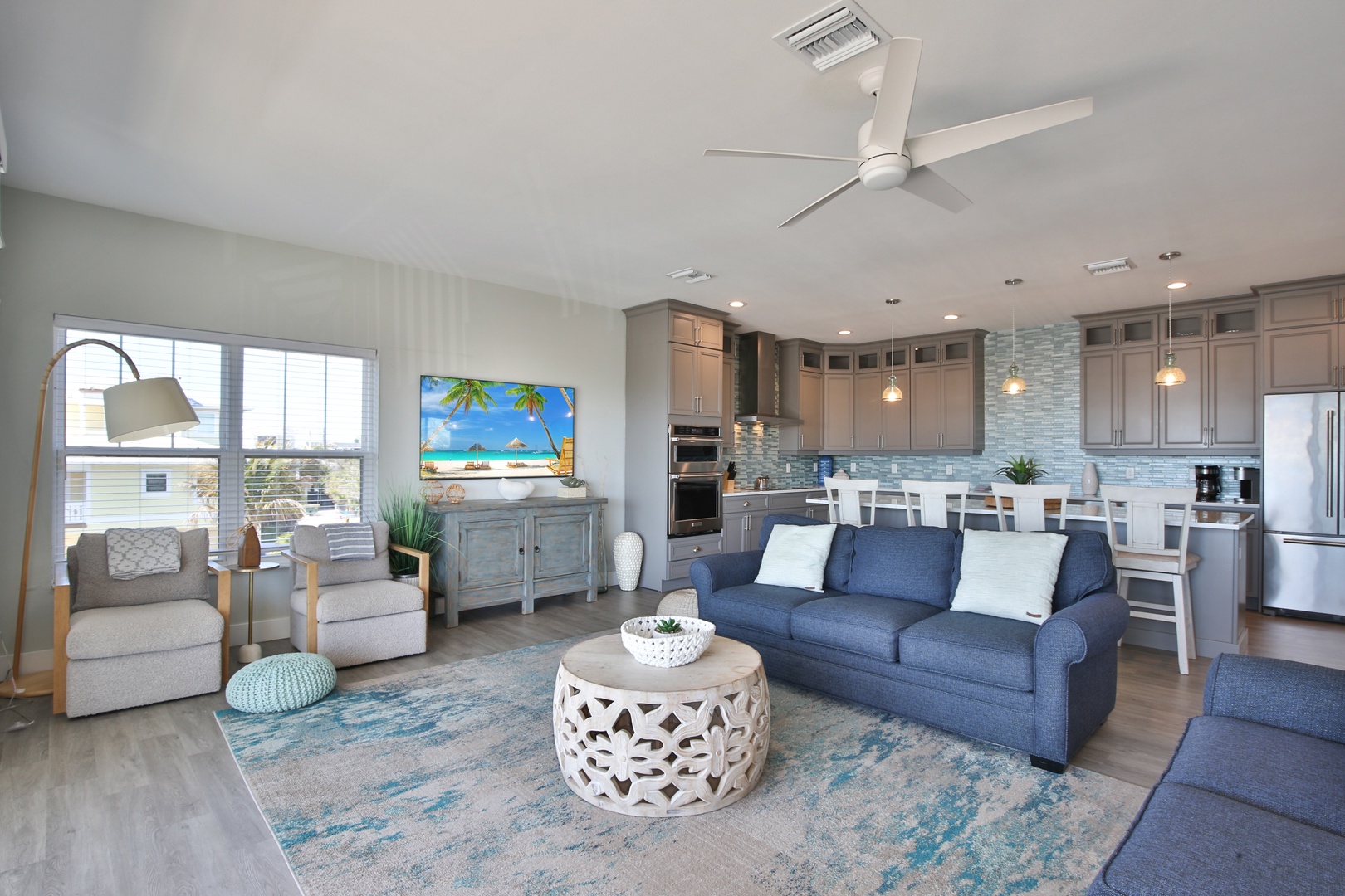 Relax in your coastal-inspired living space with plush seating, modern kitchen, and tropical artwork creating the perfect beach getaway atmosphere.