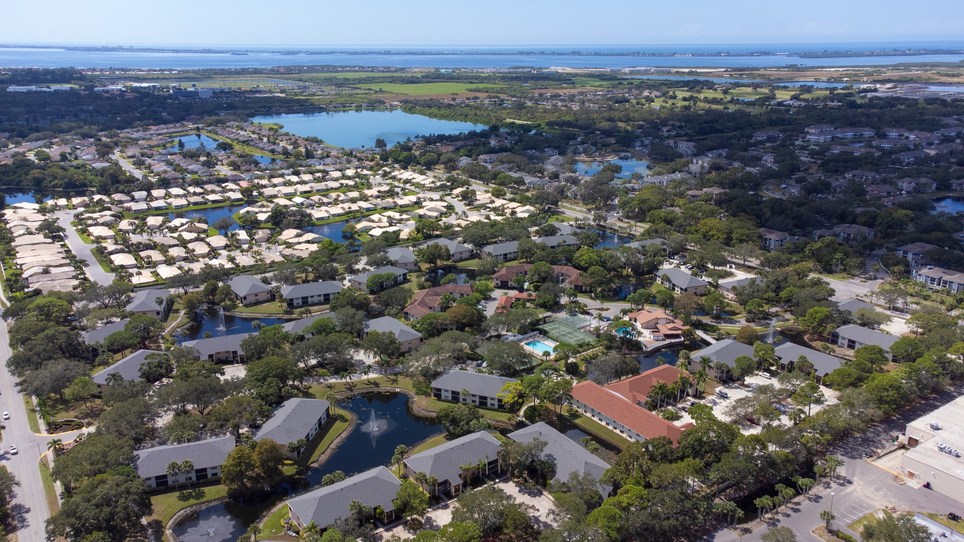 Aerial view of a sprawling residential community with lakes, pools, and lush landscaping near coastal waters.