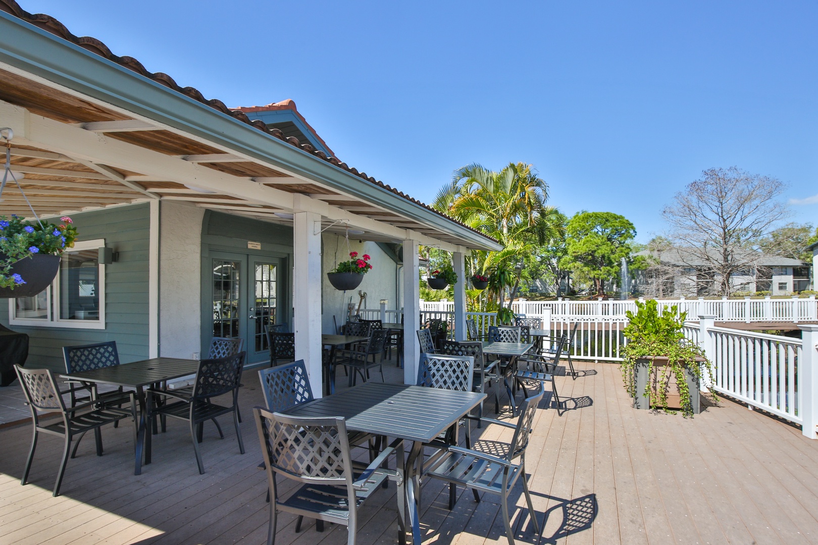 Spacious covered deck with multiple dining tables surrounded by tropical palms and lush greenery under clear blue skies.