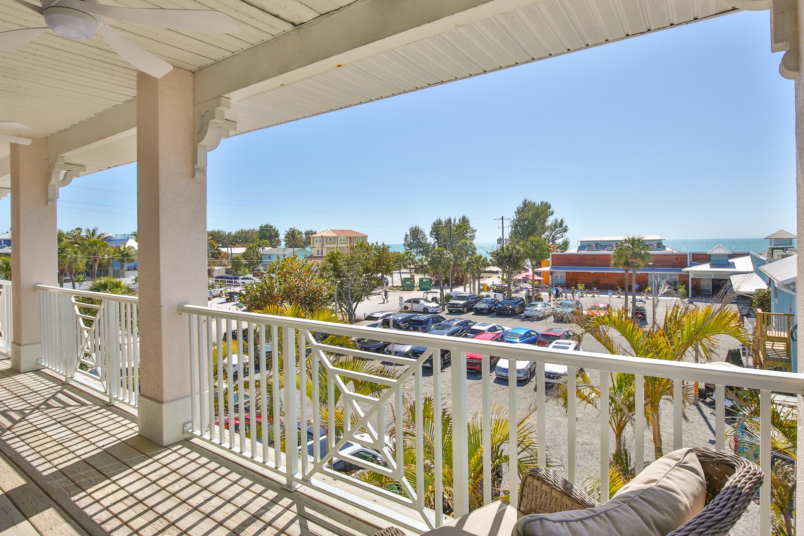 Covered balcony with white railings overlooks tropical town center. Palm trees and clear skies create a peaceful setting for morning coffee or evening relaxation.