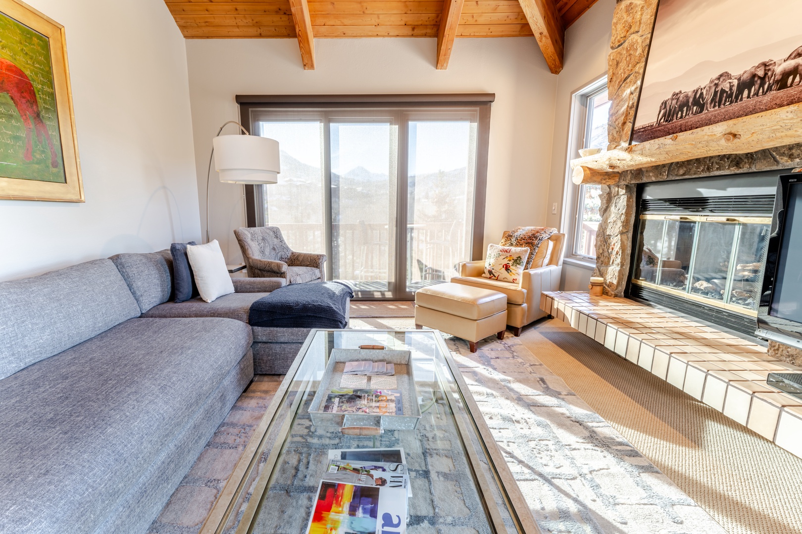 Unwind in your cozy living room with exposed beams, stone fireplace, and comfortable seating where natural light creates the perfect retreat.