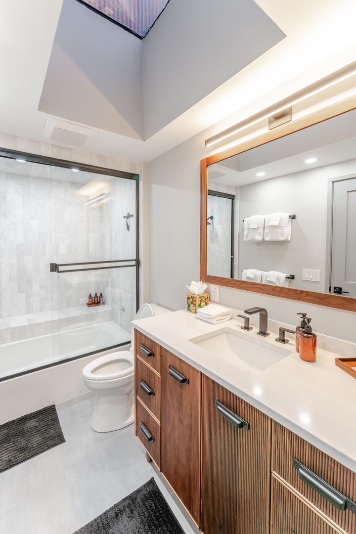 Unwind in your luxurious guest bathroom featuring a skylight, rain shower, and elegant wood vanity with premium amenities.