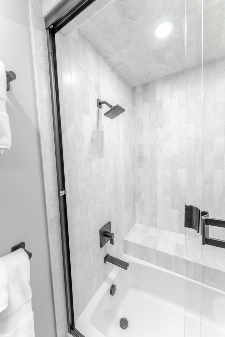 Step into your sleek guest bathroom featuring a luxurious tub-shower combo with modern fixtures and elegant marble-style tiling throughout.
