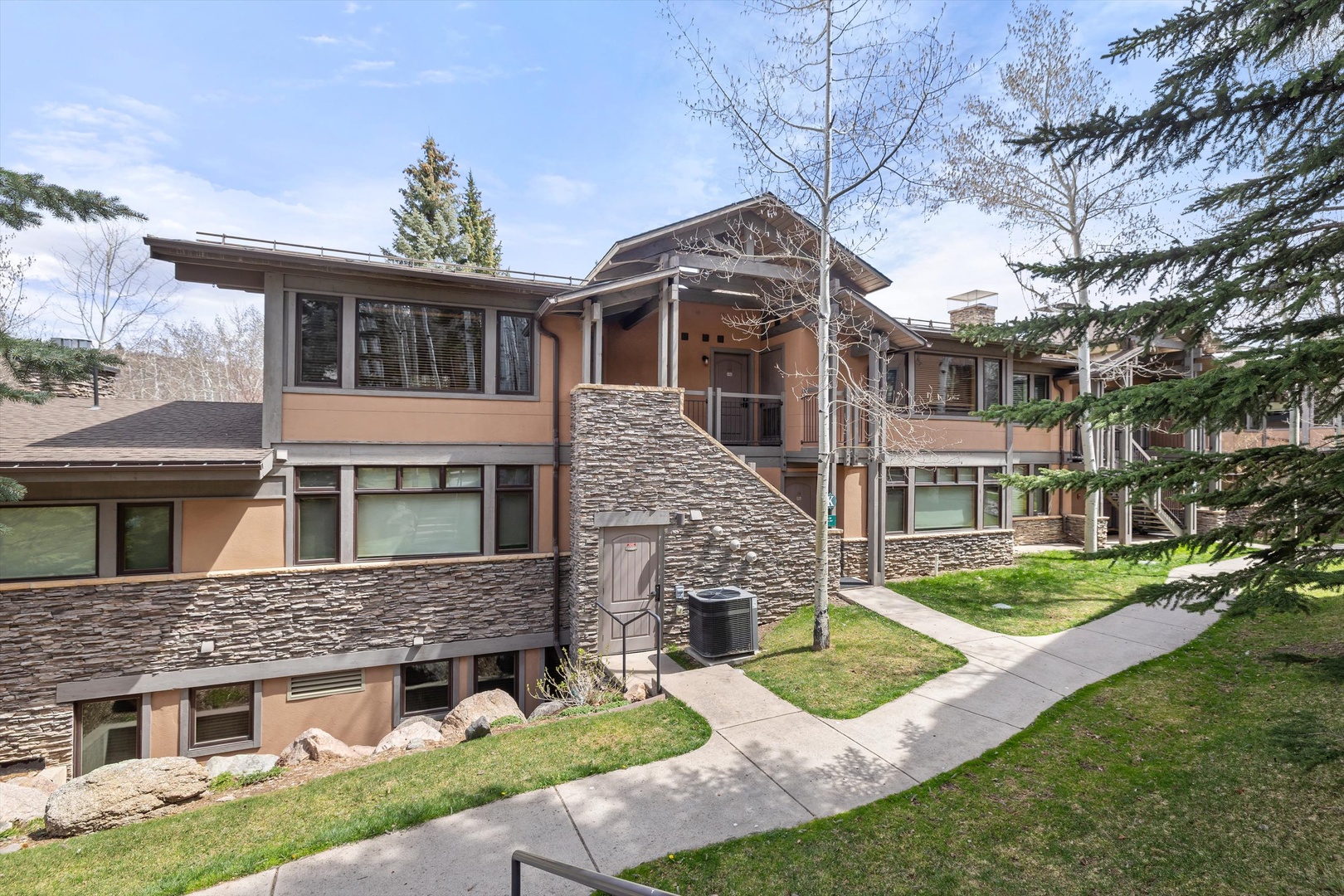 Modern multi-level property featuring stone accents and contemporary architecture, surrounded by mature evergreens and manicured lawns.