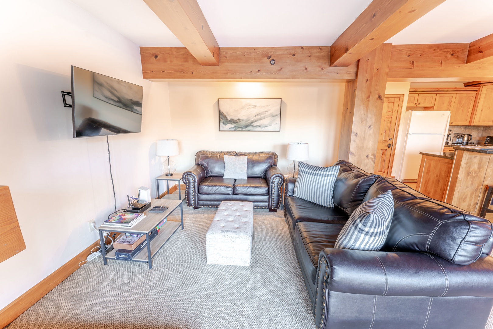 Living room with exposed wooden beams, leather sofa, and sliding glass doors to balcony. Room features a mix of modern and rustic decor.
