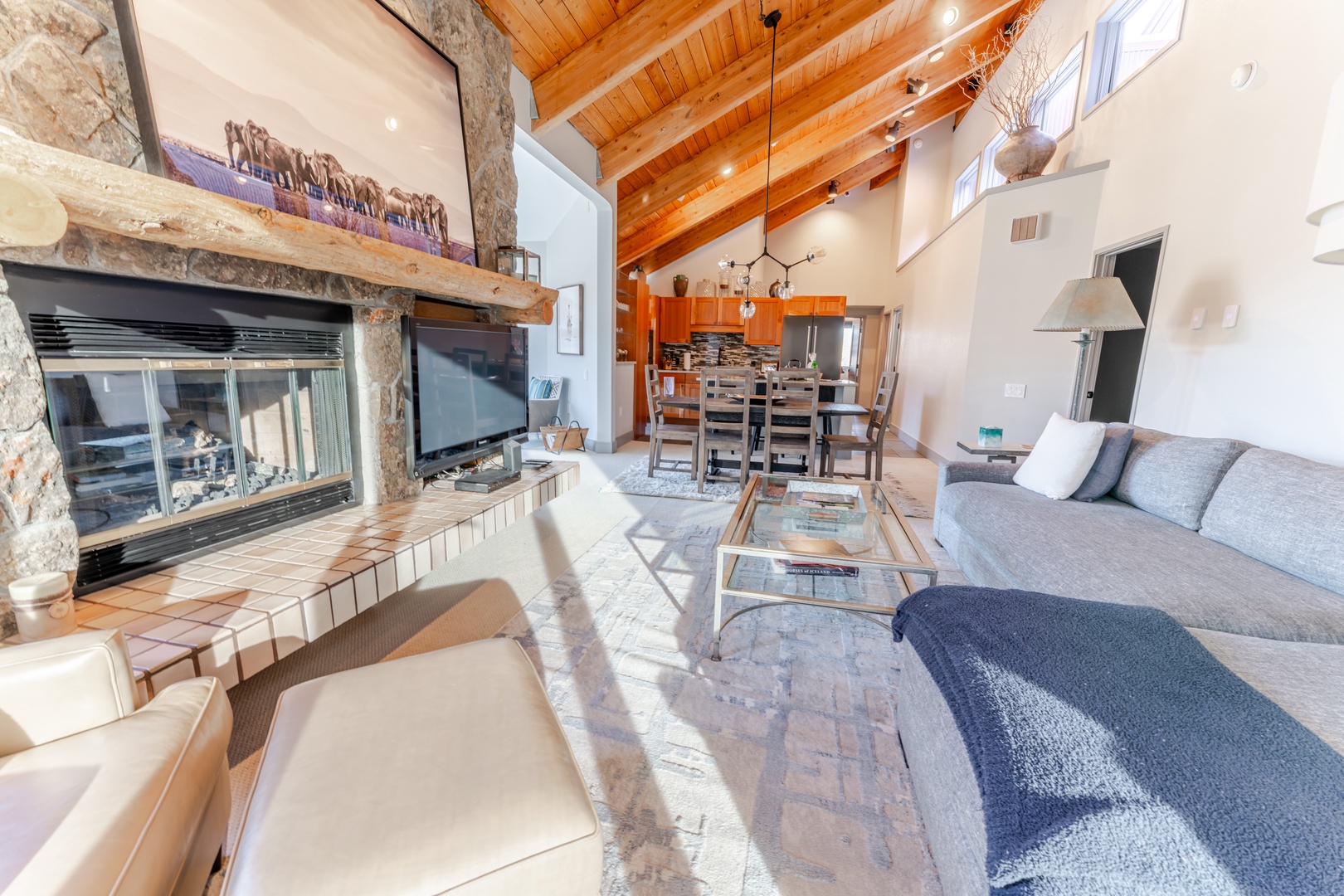 Unwind in this stunning open-concept living space where exposed wood beams meet modern comfort, complete with a stone fireplace and seamless kitchen flow.