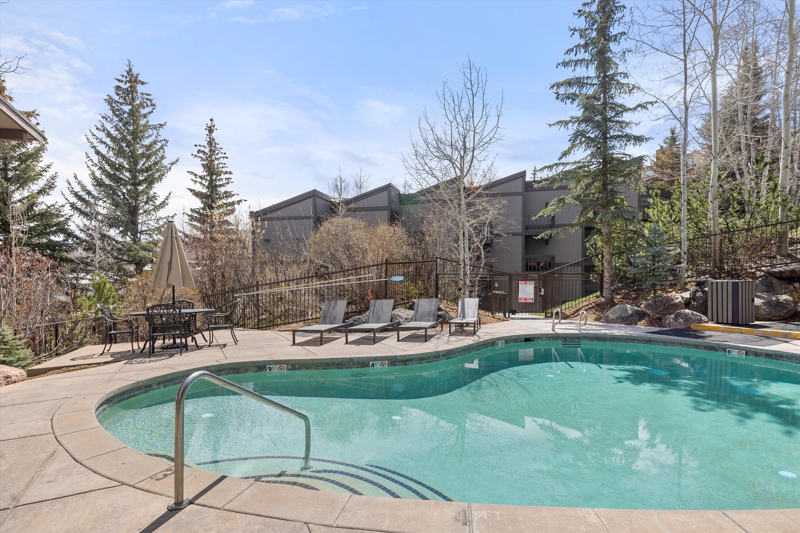Dive into the sparkling pool surrounded by towering evergreens and comfortable lounge chairs for your perfect mountain retreat relaxation.