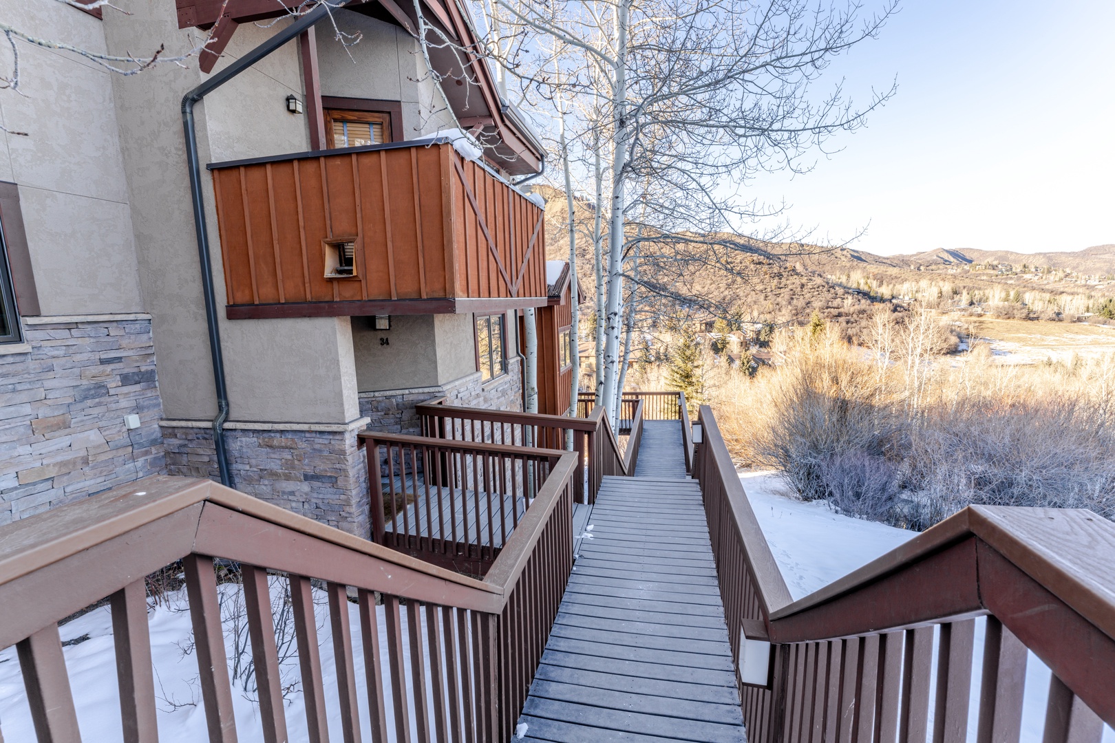 Mountain chalet with wooden walkways leading to scenic winter valley views and natural landscape surroundings.