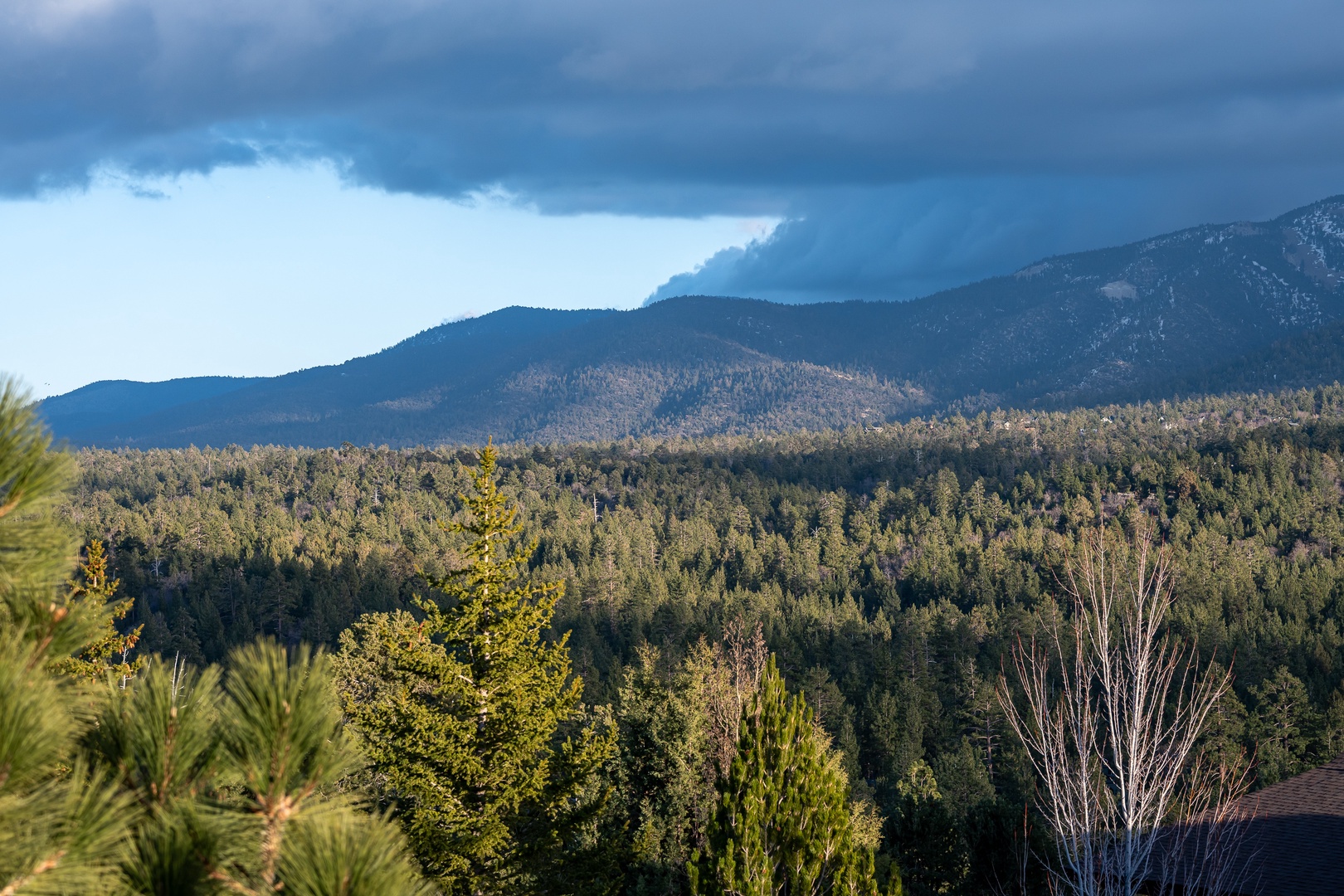 Stunning mountain landscape with rolling forested hills beneath dramatic cloudy skies in the surrounding area.