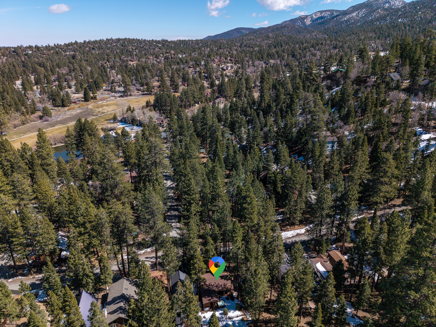Aerial view captures a vacation rental nestled among towering pines in a peaceful mountain community with snowy peaks visible in the distance.