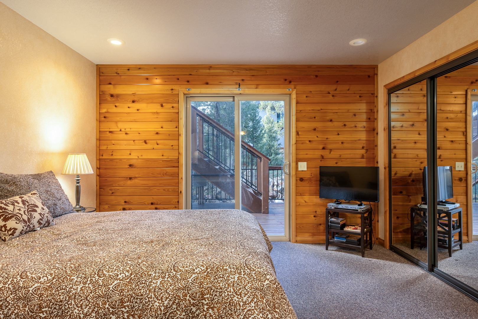 Unwind in your cozy bedroom featuring warm wood walls, a plush bed, and direct deck access for morning coffee.
