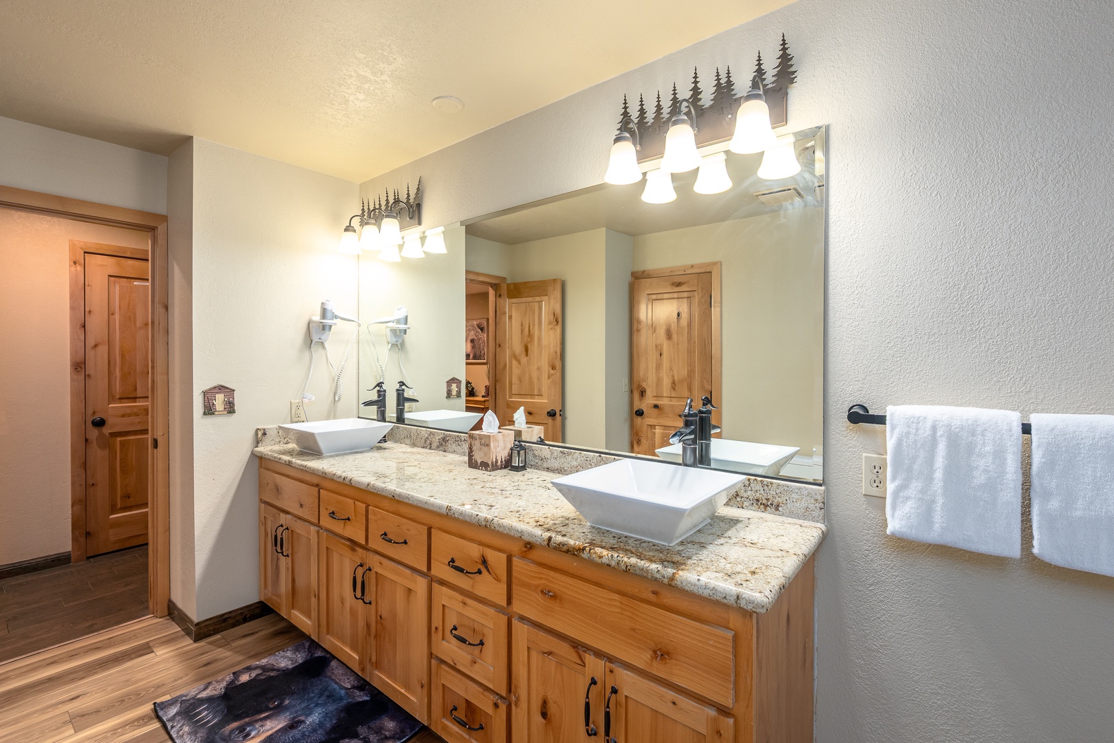Freshen up in this spacious dual-vanity bathroom featuring modern vessel sinks, granite countertops, and charming rustic pine cabinetry with nature-inspired lighting that brings the outdoors in.