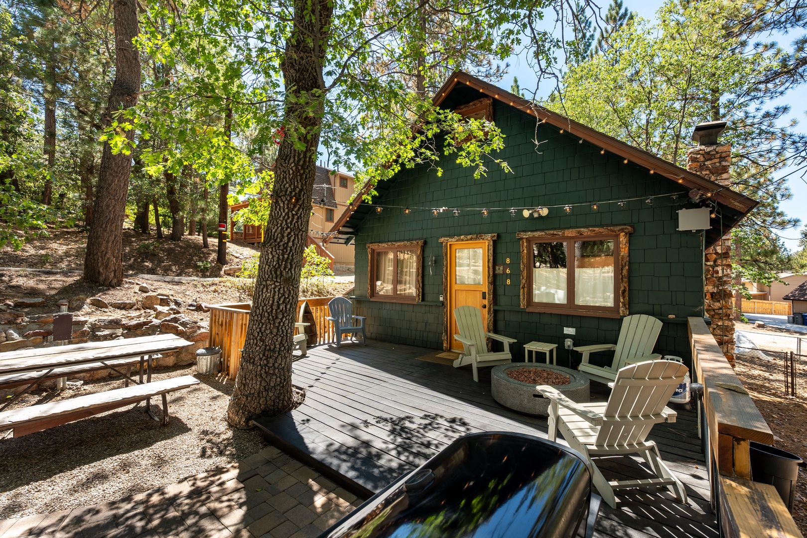 This charming forest cabin offers a cozy escape with rustic wood details and a welcoming front deck where you can relax in Adirondack chairs under towering pines.