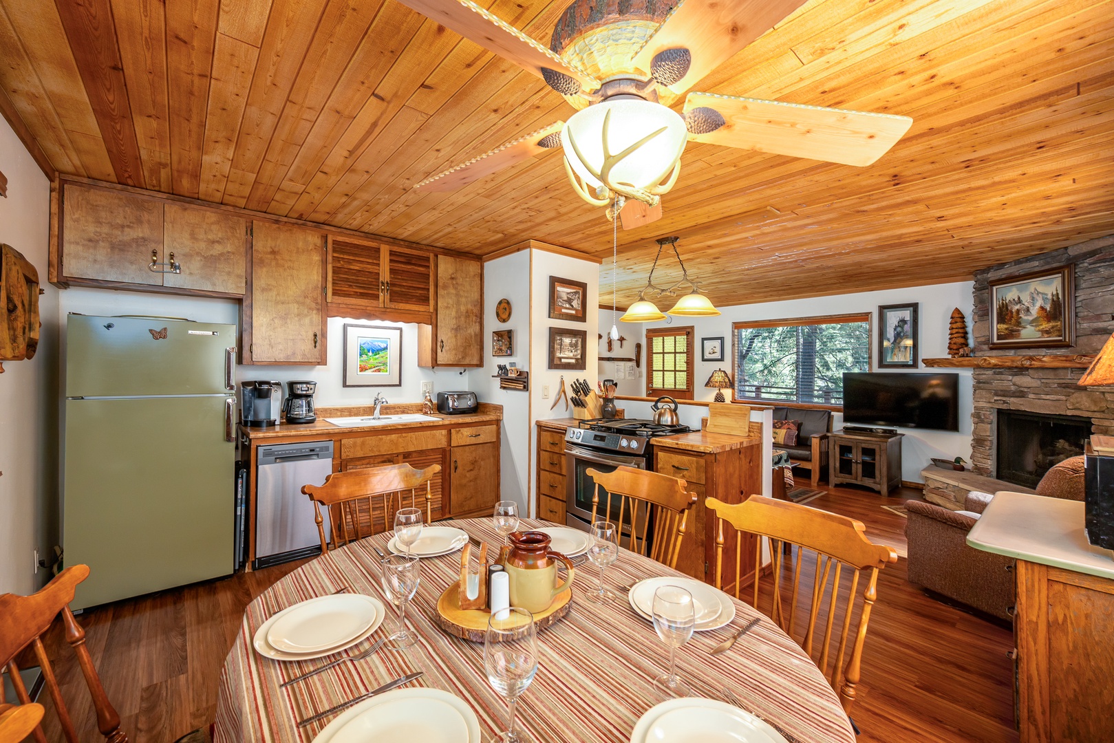 Gather around your rustic dining table in this cozy cabin kitchen where wood-beamed ceilings and stone fireplace create the perfect mountain retreat atmosphere.