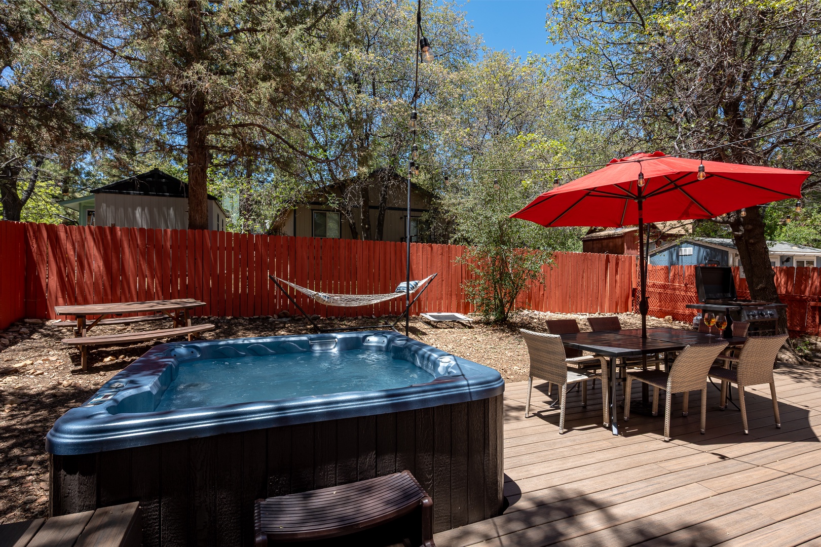Your private backyard oasis awaits with a bubbling hot tub, hammock for lazy afternoons, and a dining set under a bright red umbrella—perfect for outdoor meals and starlit evenings.
