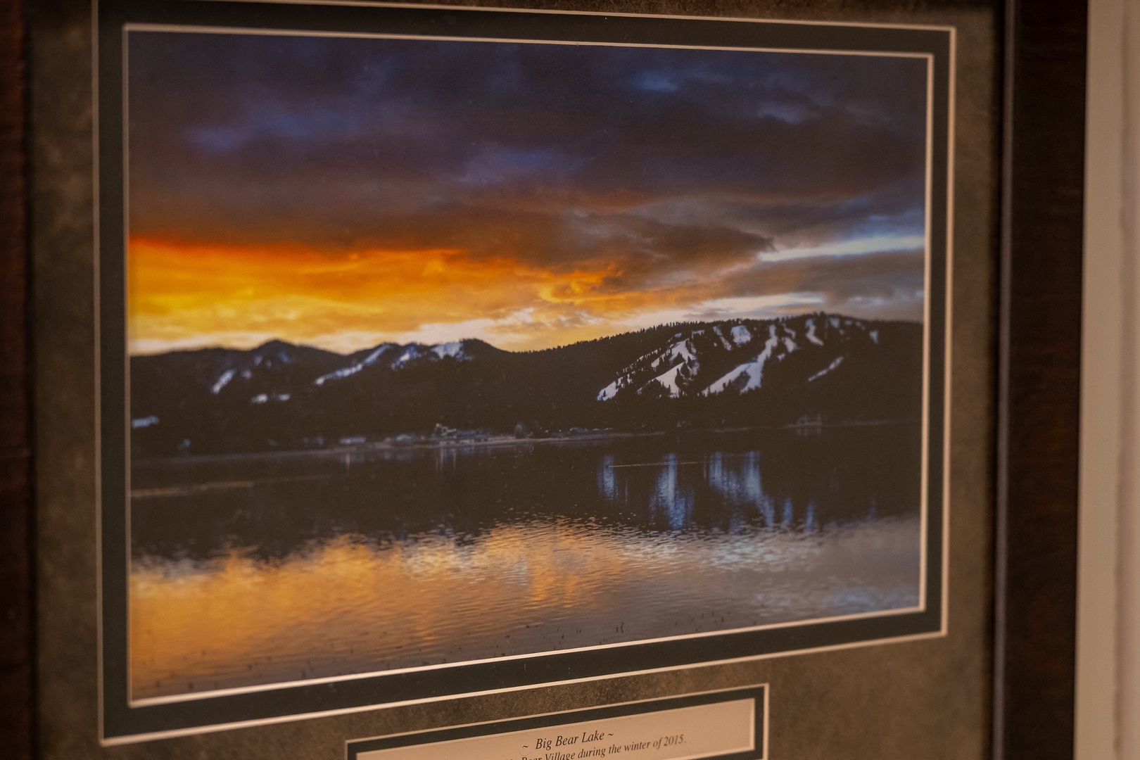 A framed photograph captures a dramatic sunset over snow-dusted mountains reflected in calm lake waters—a beautiful piece of decor enhancing the ambiance of your rental.
