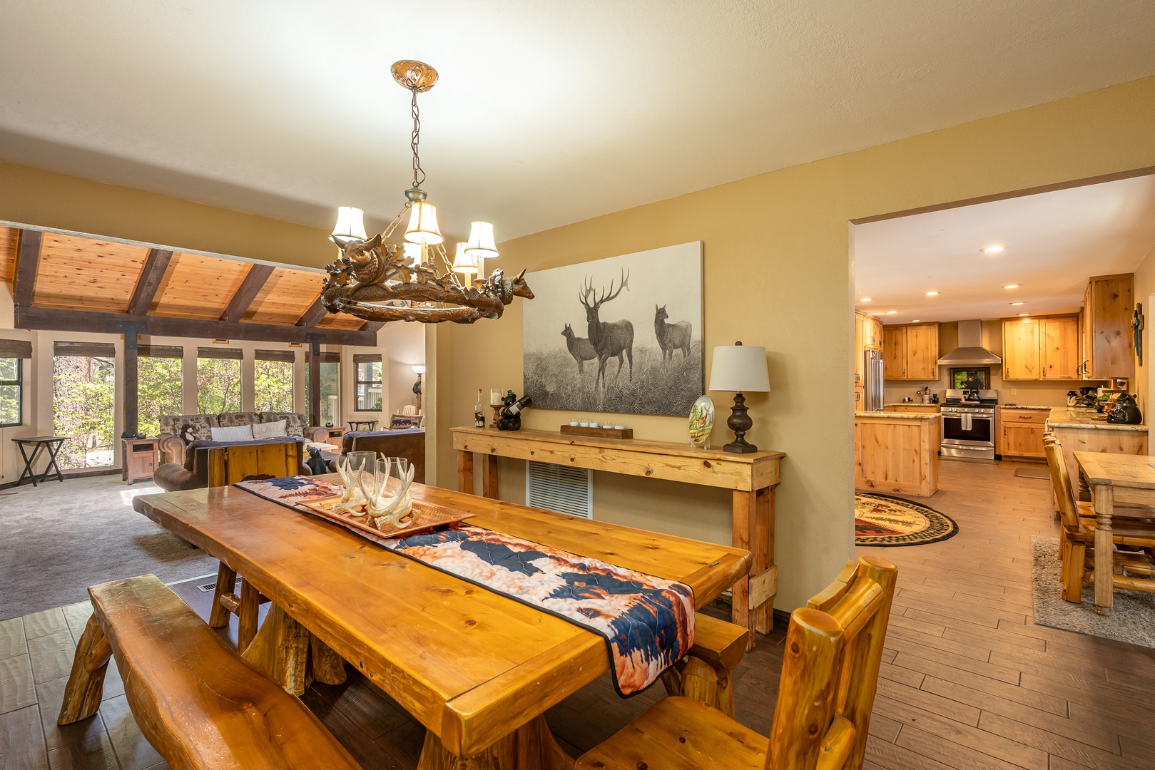 Gather around the rustic dining table under a charming antler chandelier, with warm wood finishes and an open layout flowing into your fully-equipped kitchen—perfect for memorable meals together.