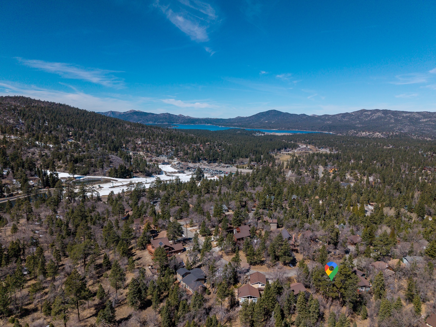 Aerial view of a mountain community nestled among pine forests, with a pristine lake and scenic mountain ranges creating a peaceful backdrop.