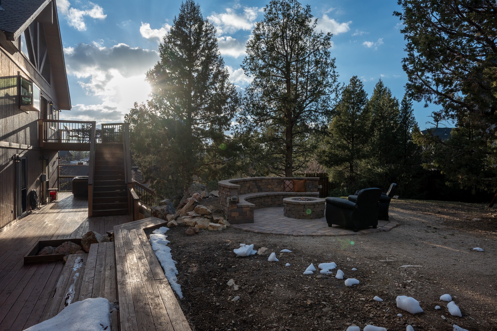A scenic mountain property featuring outdoor fire pit seating area surrounded by towering evergreens and natural landscape.