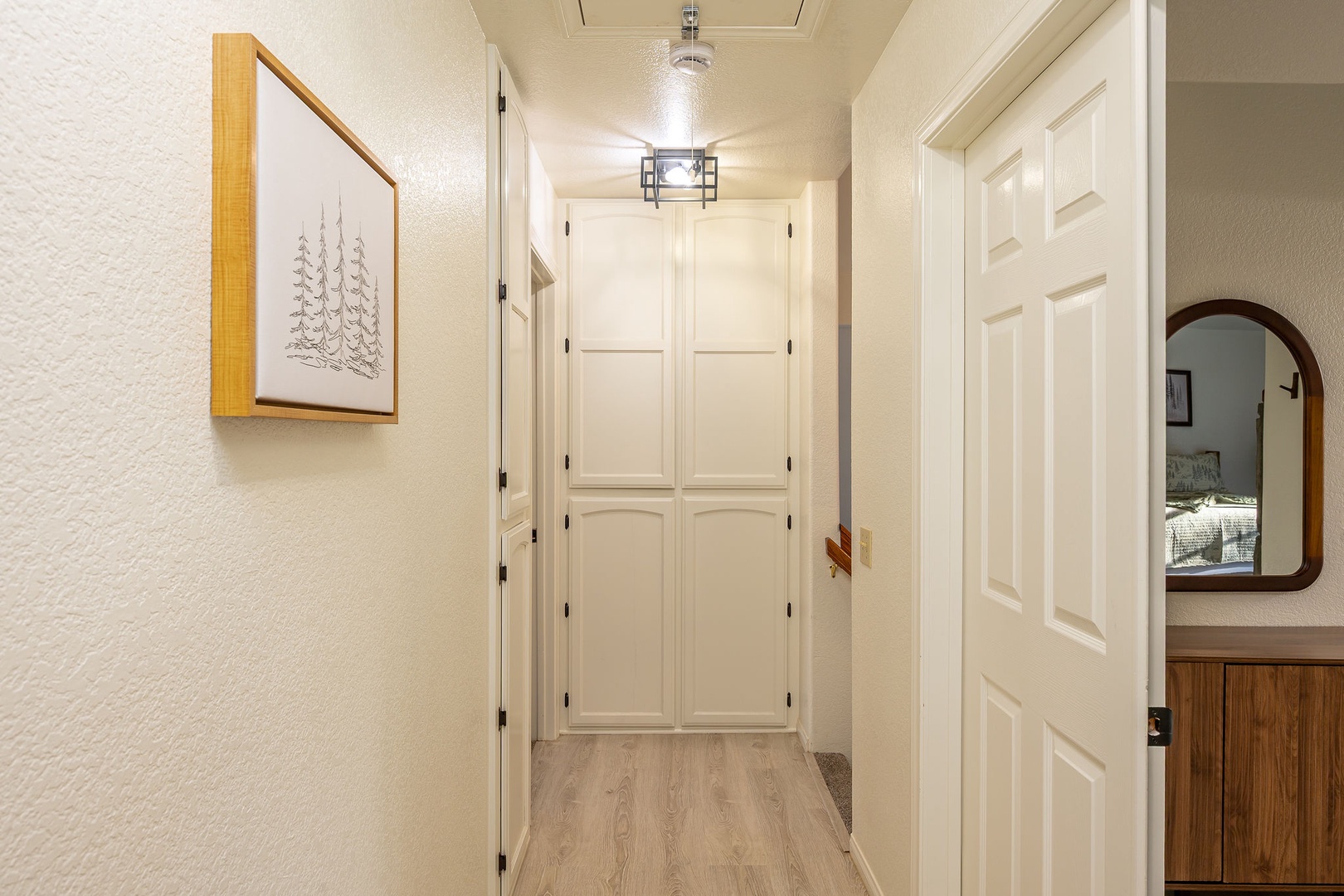 Upstairs hallway featuring clean white doors, warm lighting, and thoughtful touches like coastal artwork that create a welcoming first impression.
