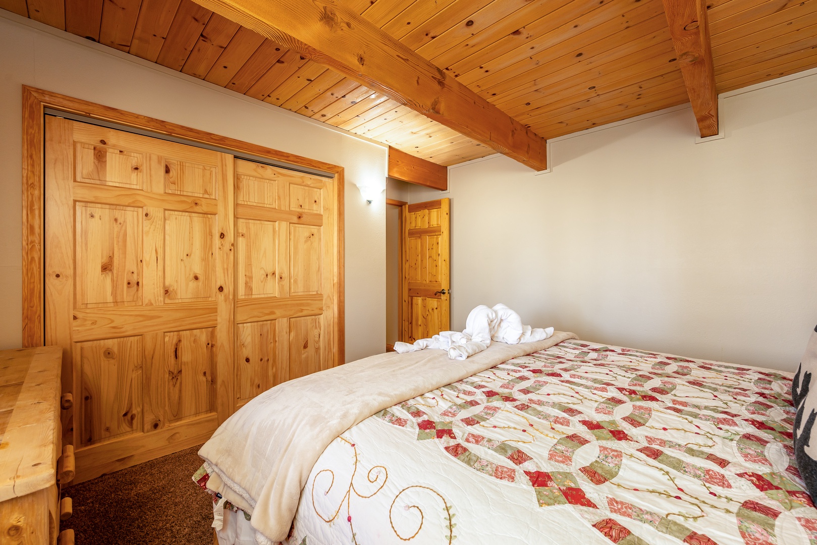 Rest peacefully under charming exposed beams in your cozy bedroom, where rustic wood meets quilted comfort for the perfect mountain retreat.