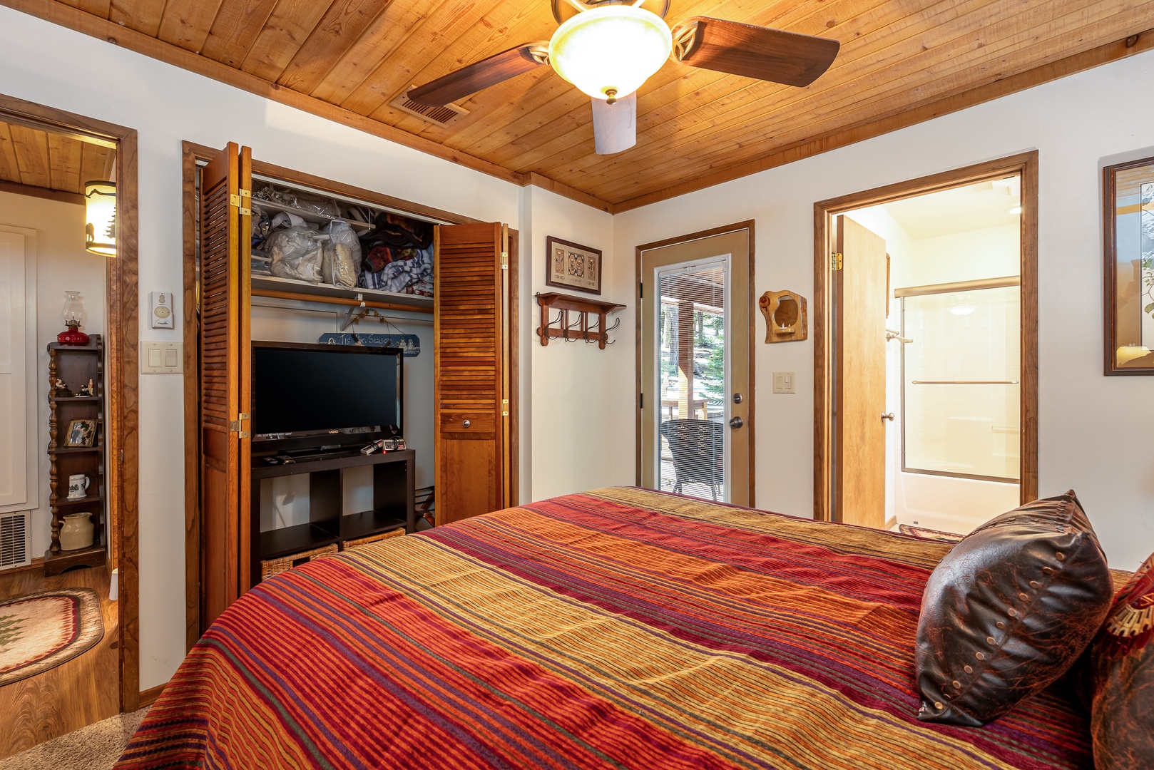 Unwind in your cozy bedroom with warm wood ceilings, a ceiling fan for comfort, and a TV for relaxation. Natural light and thoughtful touches create a welcoming retreat after your adventures.