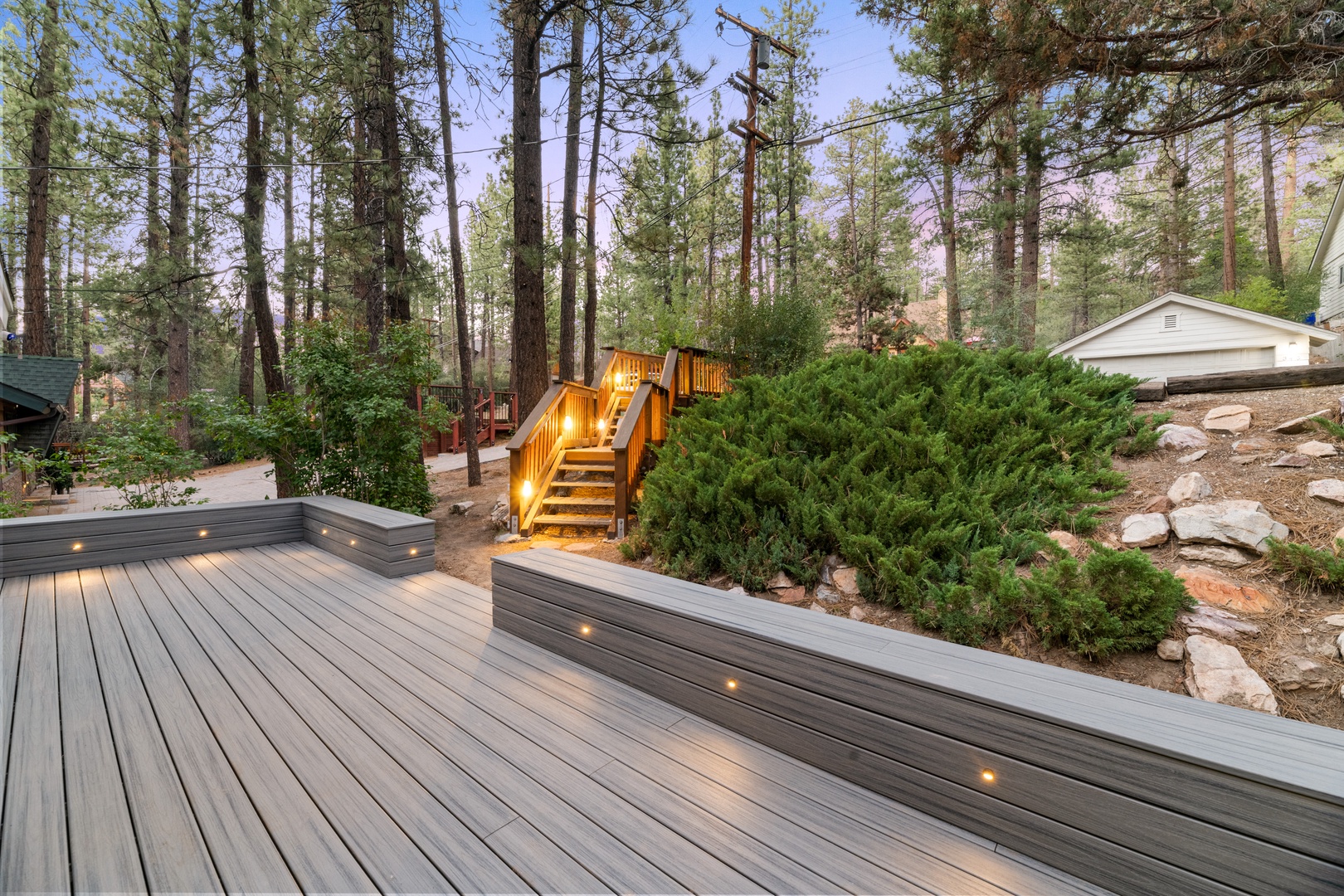 A spacious outdoor deck nestled among towering pines, featuring built-in lighting and multi-level design perfect for your mountain retreat evenings.