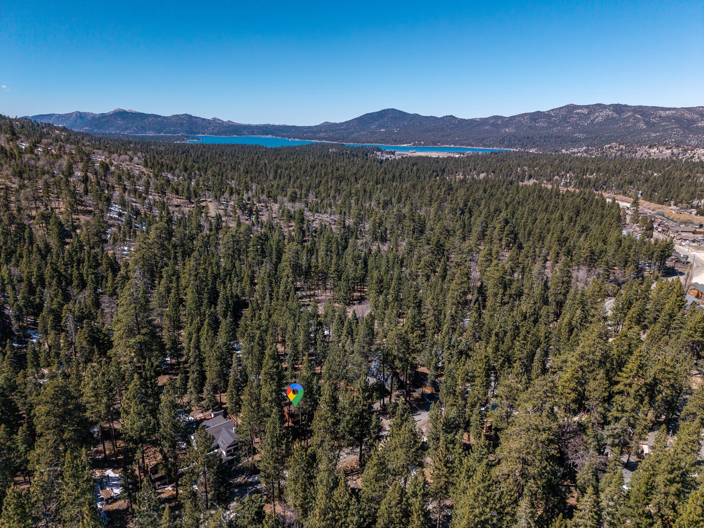 Aerial view showcasing the property nestled among evergreen forest with a stunning alpine lake and mountain ranges in the distance.